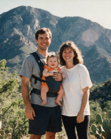 A young family — mum, dad and their baby — smiling together on a mountain hike