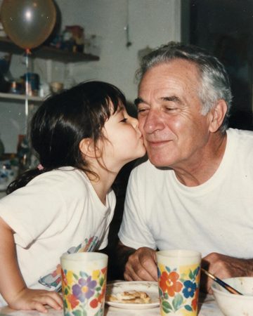 A little girl kissing her grandfather on the cheek at the kitchen table